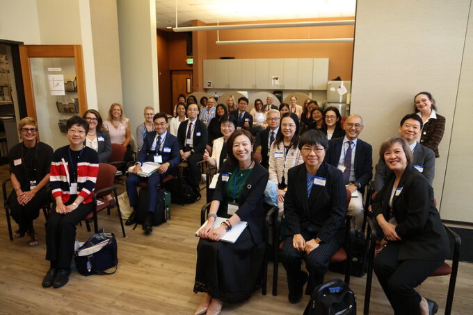 Room full of individuals in business attire seated in lines of chairs, facing the camera and smiling.