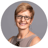Cropped headshot of white presenting woman with short hair and dark framed glasses smiles into the camera