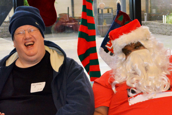 A middle age man with glasses and a beanie laughs next to santa