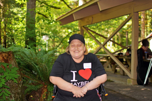 A blonde woman smiling while sitting on her walker outside