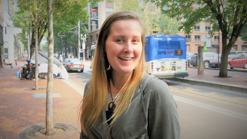 Young beautiful female with long hair and smile standing on the sidewalk downtown with a bus in the background