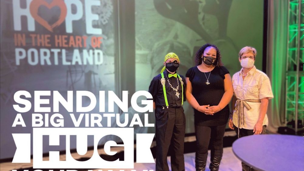 Picture of three people in masks in front of an electronic screen with the words "Sending a big virtual hug your way"