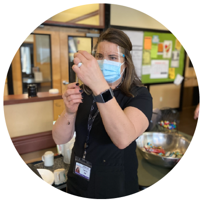 A nurse in protective gear inserts a syringe into a bottle of vaccine