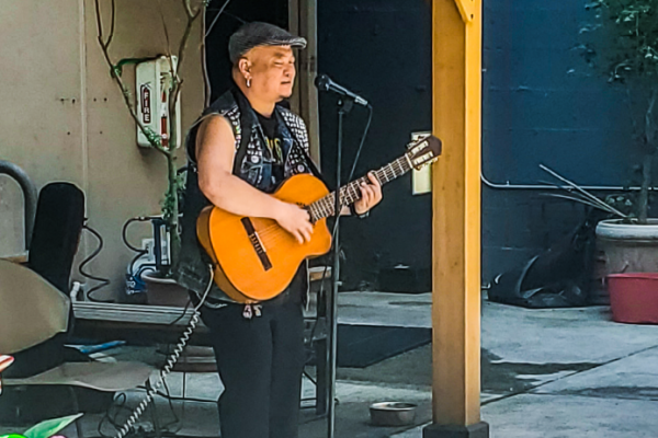 Middle-aged asian map with hat and sleeveless shirt singing and playing the guitar in front of a microphone outdoors