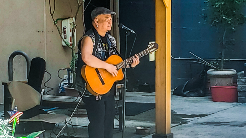 Middle-aged asian map with hat and sleeveless shirt singing and playing the guitar in front of a microphone outdoors