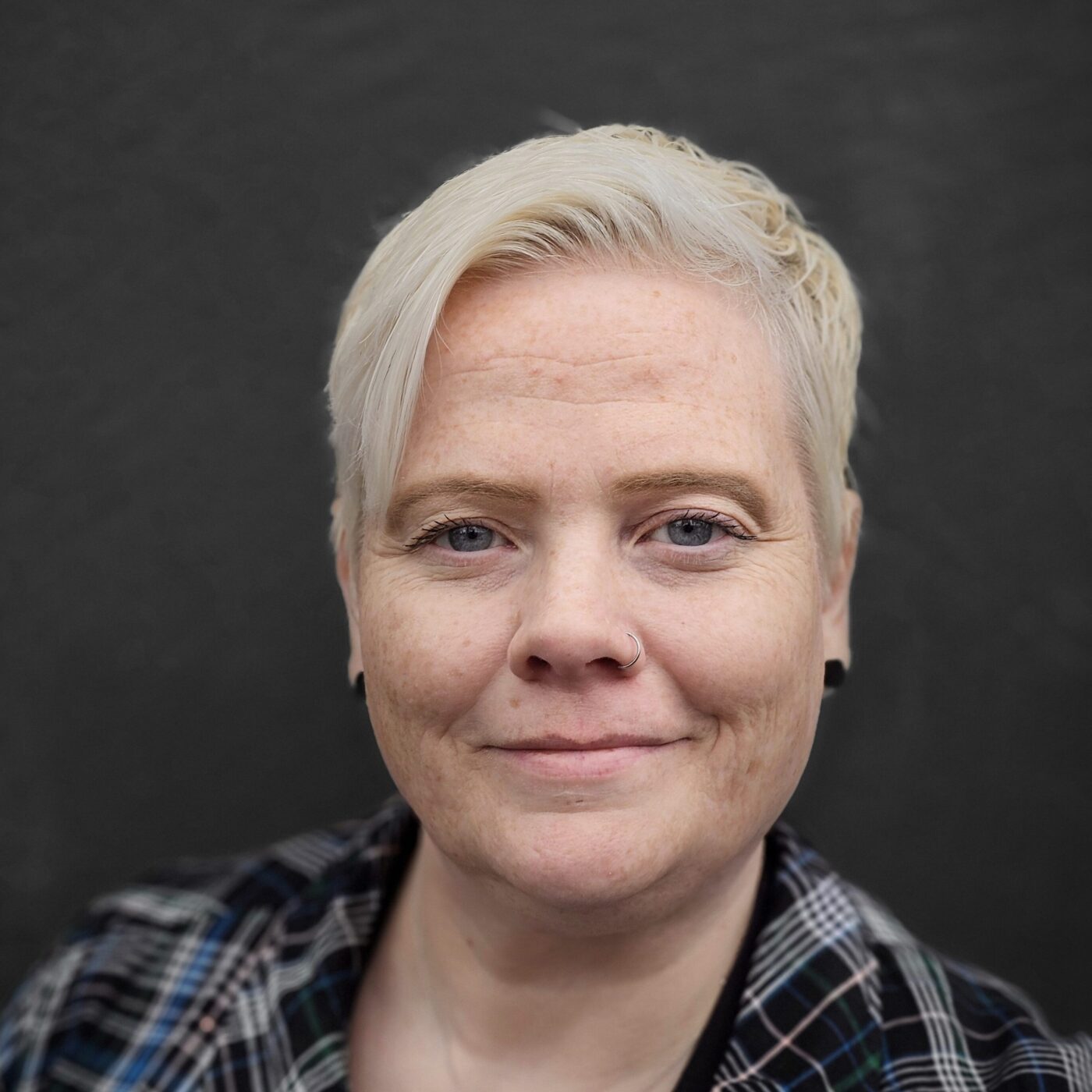 Headshot photo of white woman with short, close-cropped white hair, smiling faintly into the camera in front of dark background