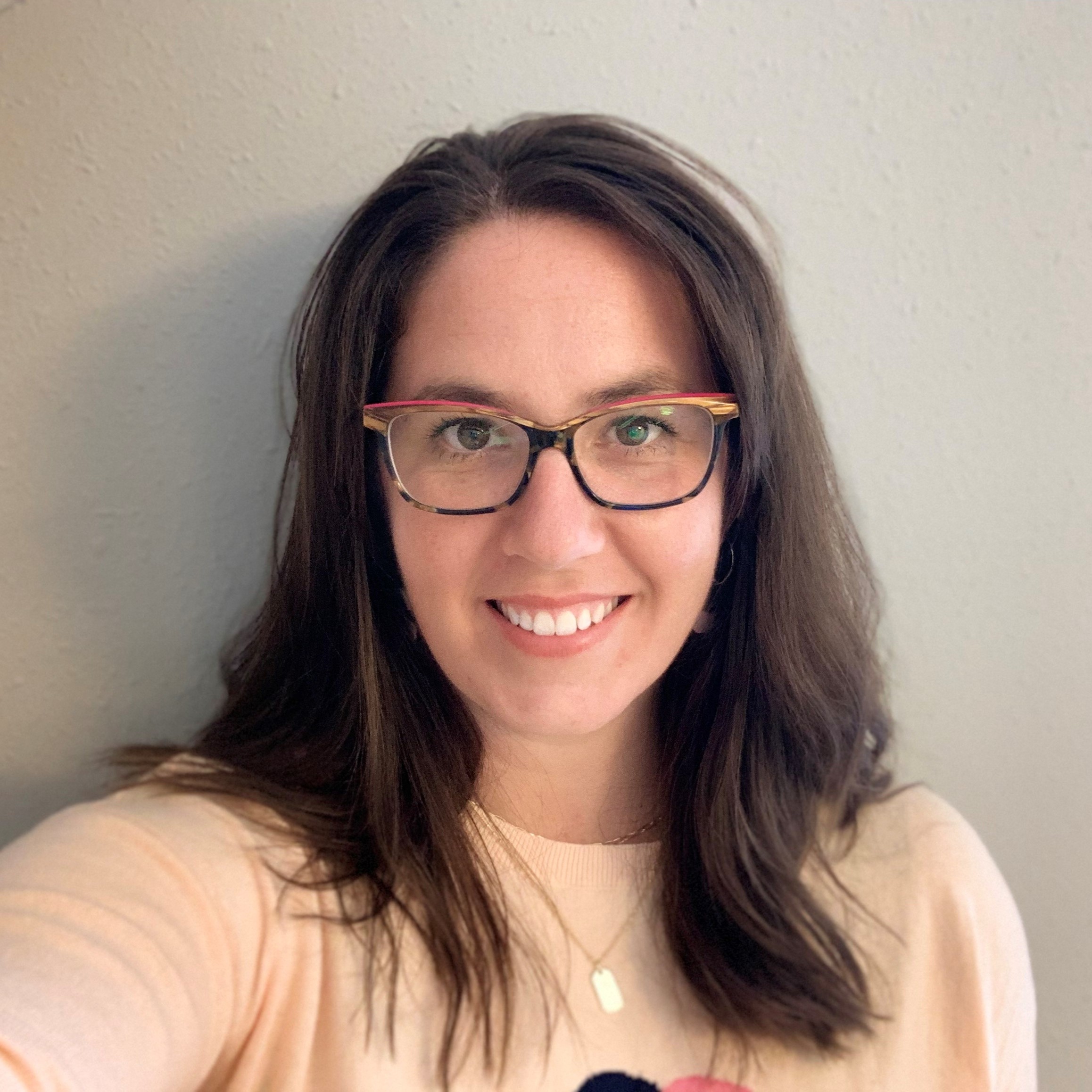white woman with shoulder-length brown hair, wearing glasses smiles directly at the camera