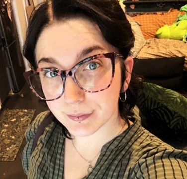 White woman looking directly into camera, with dark hair and large rimmed tortoise-shell glasses