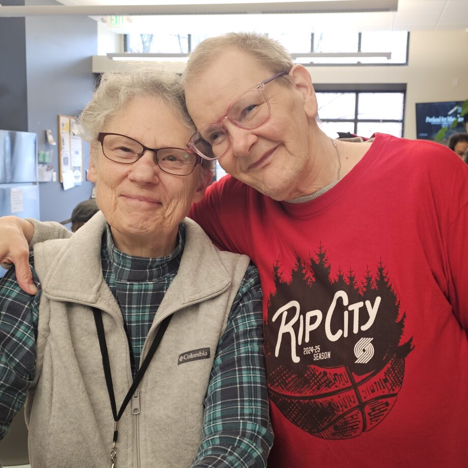 Older white man stands with arm around shoulders of older white woman, both smile directly to the camera and have the sides of their foreheads pressed together