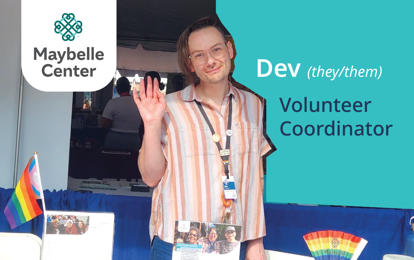 White younger person with short brown hair stands at a table, waving to the camera. The image has been edited to include a block of color along one side, over which reads 'Dev (they/them), Volunteer Coordinator' and on the other side a white block of color over which is the Maybelle Center logo